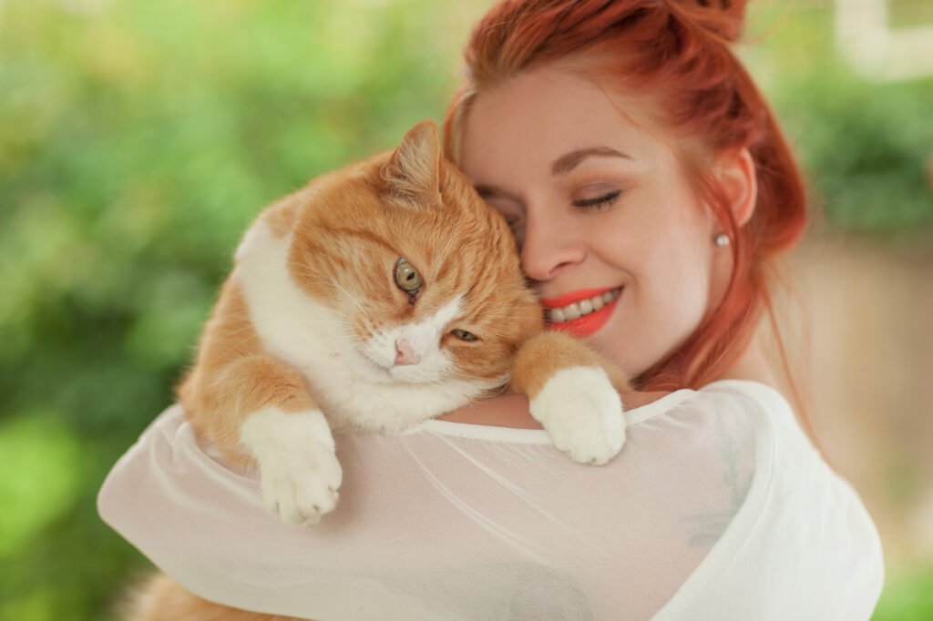 Beautiful young woman cuddling with cute red cat in her arms
