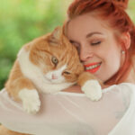 Beautiful young woman cuddling with cute red cat in her arms