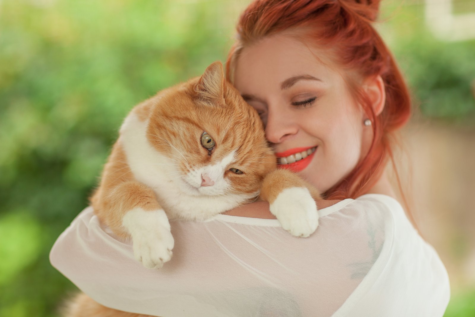 Beautiful young woman cuddling with cute red cat in her arms