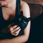 Black cat: A young woman lovingly cuddles a black cat indoors, showcasing their bond.