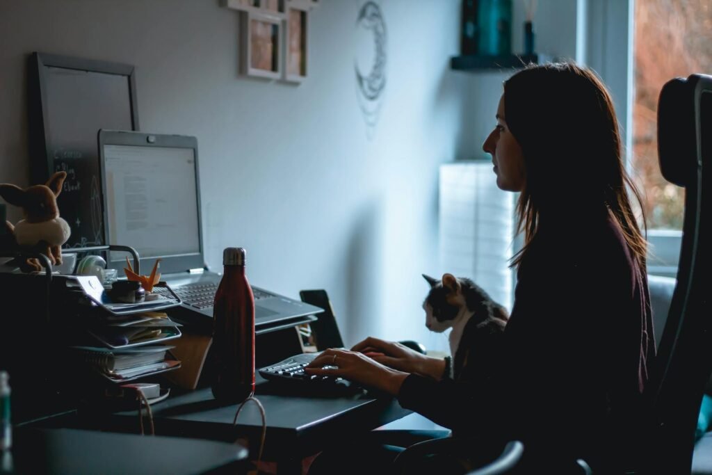 Silhouette of a woman working at her desk with a cat nearby in a cozy home office setup.