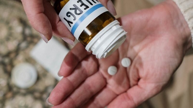 Hands holding an open bottle labeled "Allergy" and two small pills, highlighting medication for allergy management.