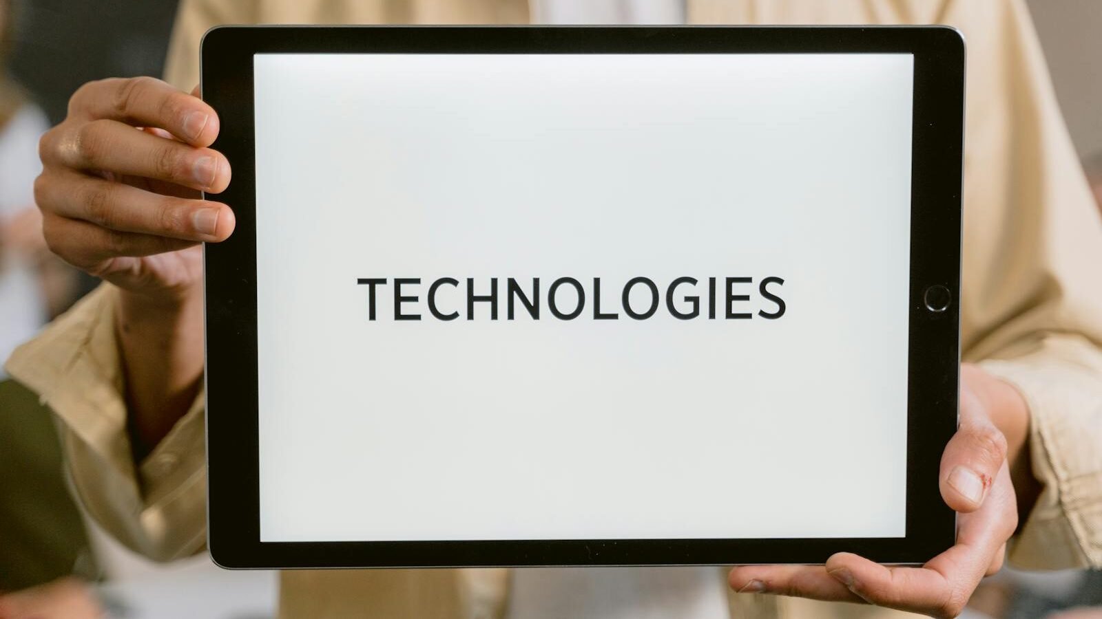 A person holding a tablet displaying the word "TECHNOLOGIES" on a bright white screen. The background is blurred, focusing attention on the tablet and its message.