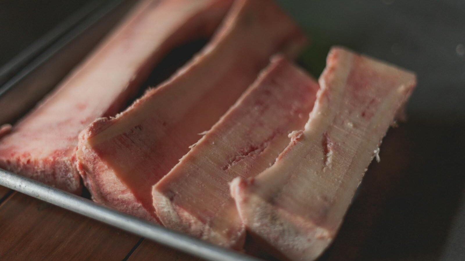 Close-up of raw bone marrow slices arranged on a metal tray, showcasing a nutrient-rich component often included in carnivorous diets. The texture and natural pink hues are prominently visible.