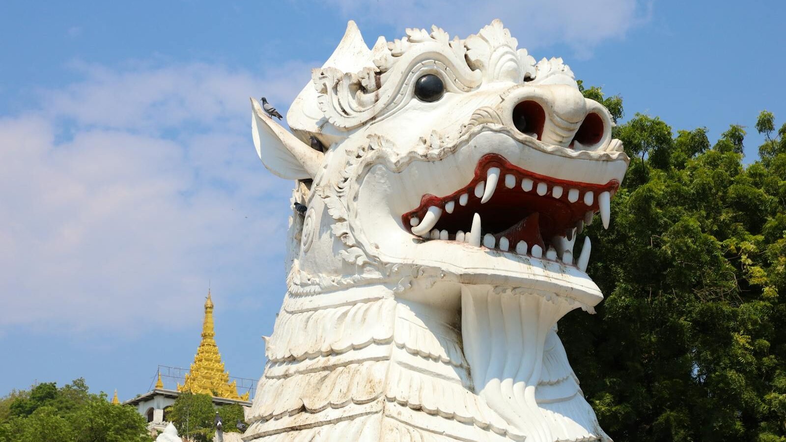 A white lion statue with intricate details, symbolizing strength and protection in mythology, set against a backdrop of blue sky and greenery