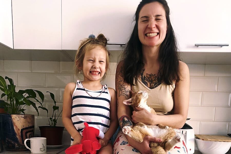 A happy mother and daughter sit on a kitchen counter with their cat, showcasing family joy.