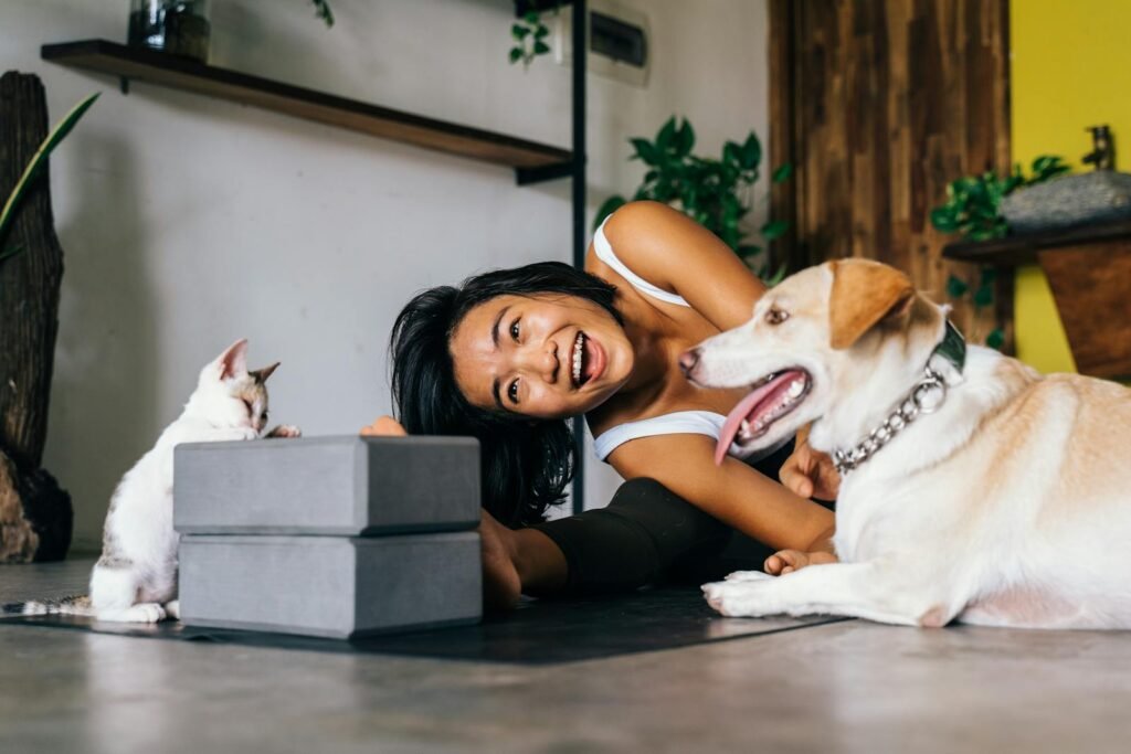 cat relationship: Smiling woman practicing yoga indoors with her dog and cat, embracing a healthy lifestyle.