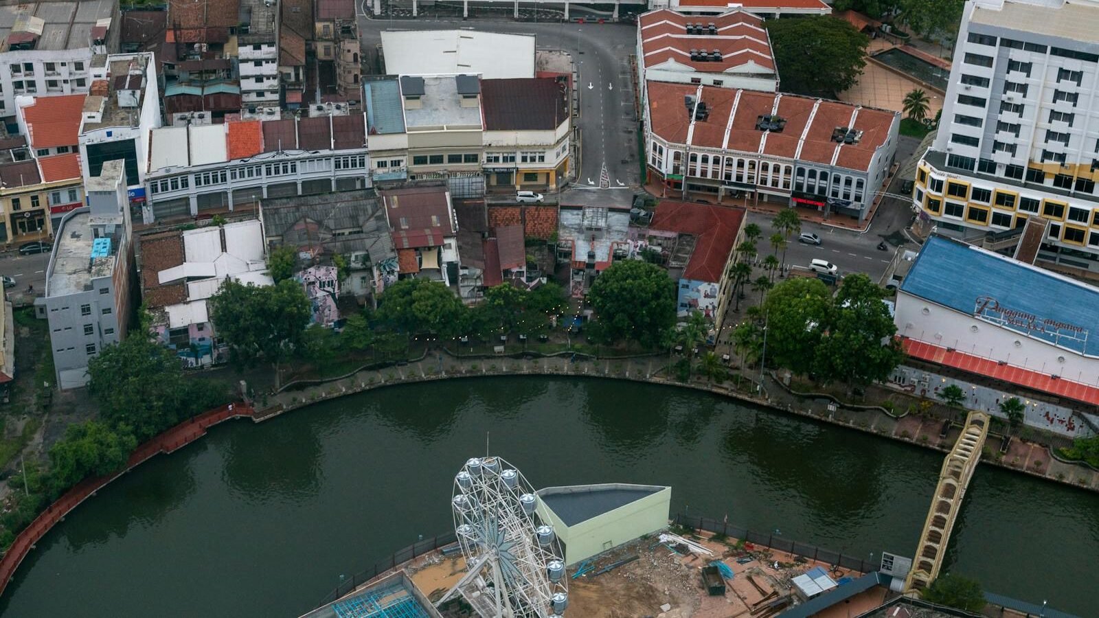 An aerial view of a colonial-style town with red-roofed buildings and modern structures surrounding a river, showcasing historical and architectural influences tied to transatlantic voyages and colonialism.