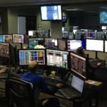 A bustling control room with people working on multiple computer monitors.