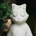 A tranquil cat figurine surrounded by greenery in a rustic garden.