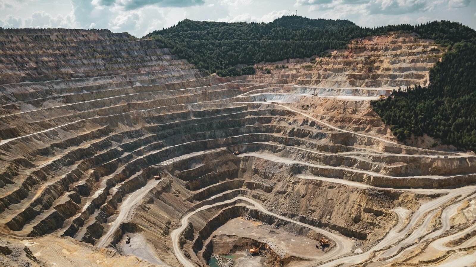 A large open-pit mine carved into the landscape, surrounded by remnants of forested hills, illustrating the environmental impact of deforestation and land degradation.