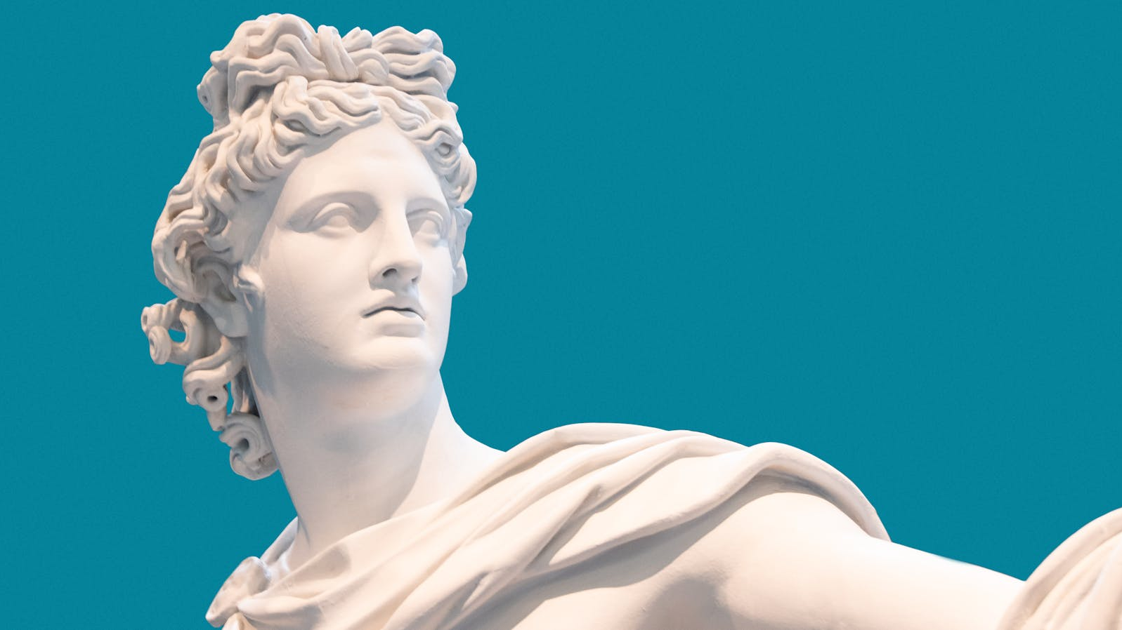 A white marble statue of a Roman or Greek aristocratic figure with flowing curls and draped clothing, set against a solid teal background, symbolizing classical art and nobility.