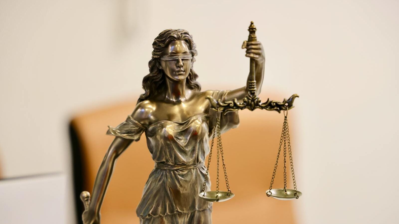 A bronze statue of Lady Justice holding scales, symbolizing fairness and impartiality, set against a neutral background, representing legal and regulatory challenges in governance and law
