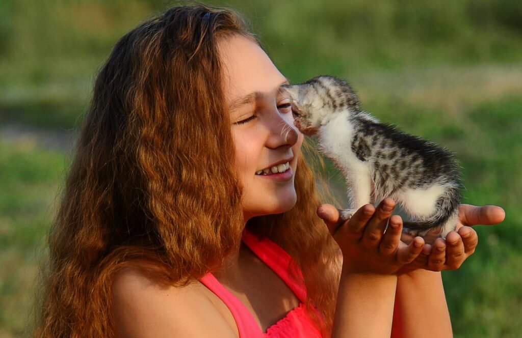 Smiling young girl holding a cute kitten outdoors, enjoying a warm sunny day.