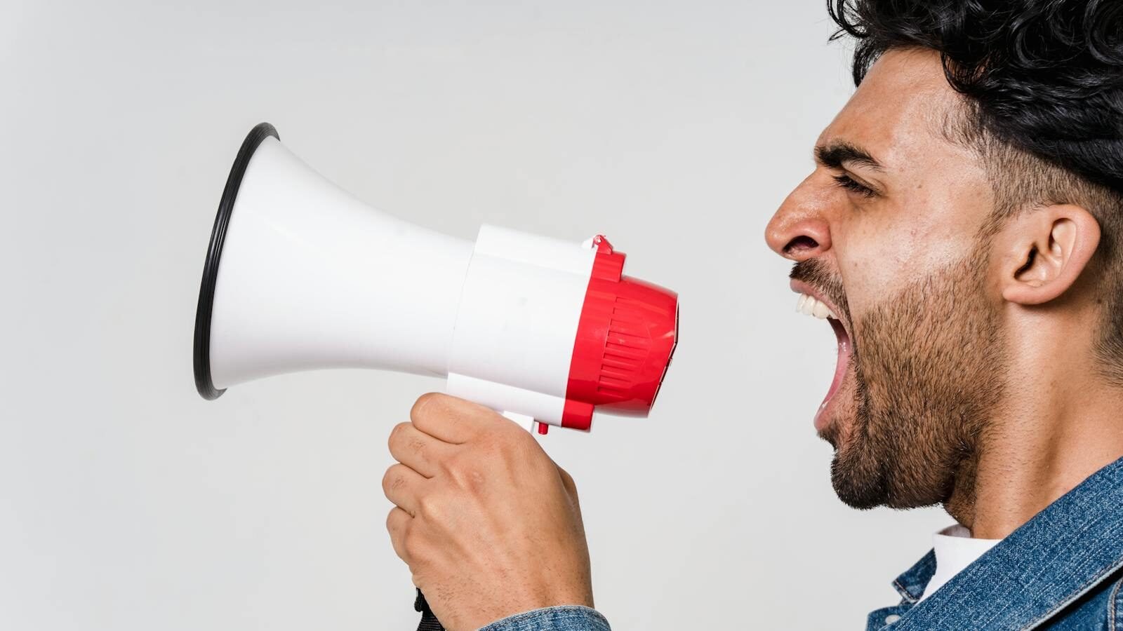 A man holding a megaphone, shouting with an expressive face, symbolizing the significance of sound in communication and interaction.
