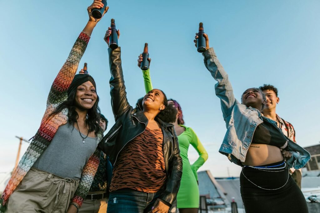 A happy group of diverse friends celebrating outdoors, raising their drinks against a clear sky.
