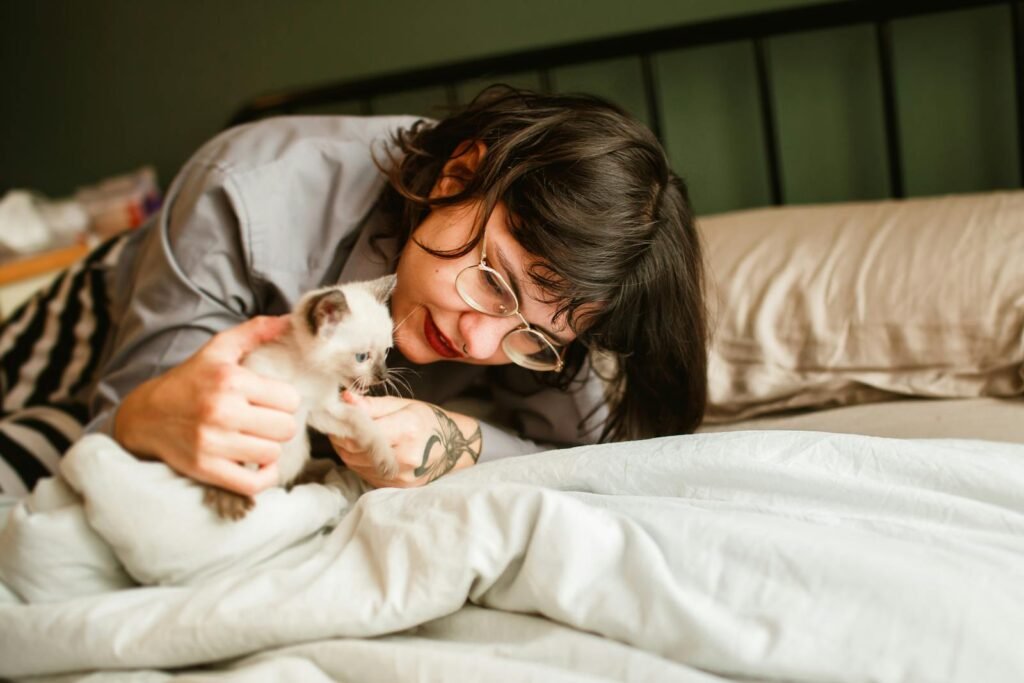 A woman lovingly playing with her Siamese kitten on a bed.