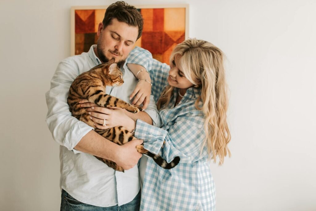 A couple happily embracing their tabby cat indoors, showcasing warmth and affection.