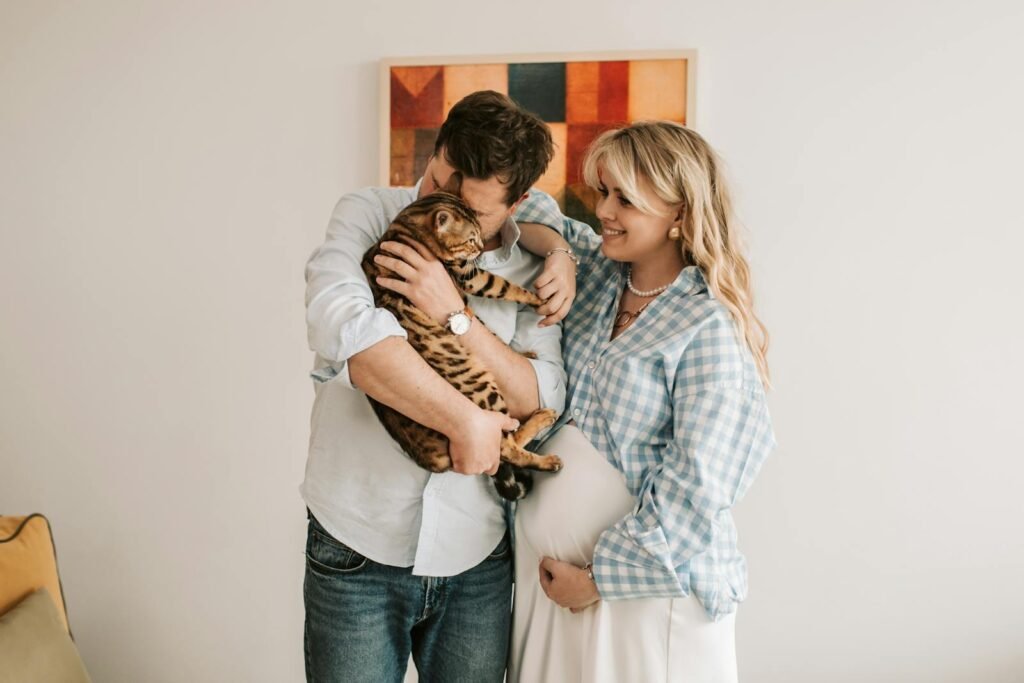 cat relationship: A joyful expecting couple with their Bengal cat, sharing a moment of affection indoors.