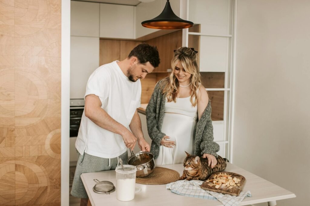 cat relationship: A pregnant couple bonding in a modern kitchen with their cat nearby and enjoying food preparation together.