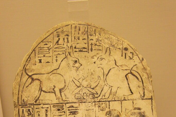 An ancient Egyptian limestone tablet featuring hieroglyphics and cat depictions, highlighting the cultural and spiritual significance of cats in ancient Egypt.