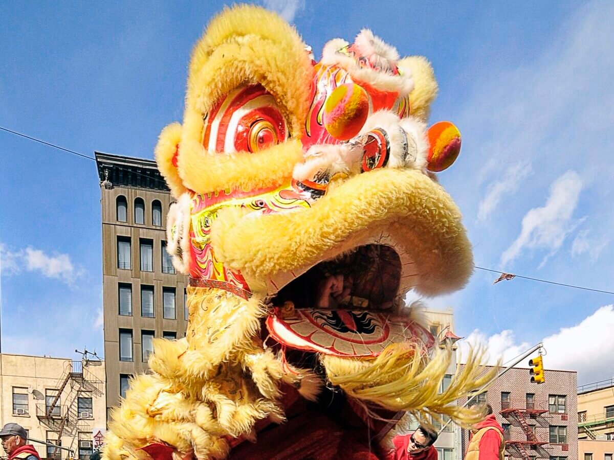 A vibrant Chinese lion dance performance taking place on a city street, with performers dressed in red and yellow traditional costumes.