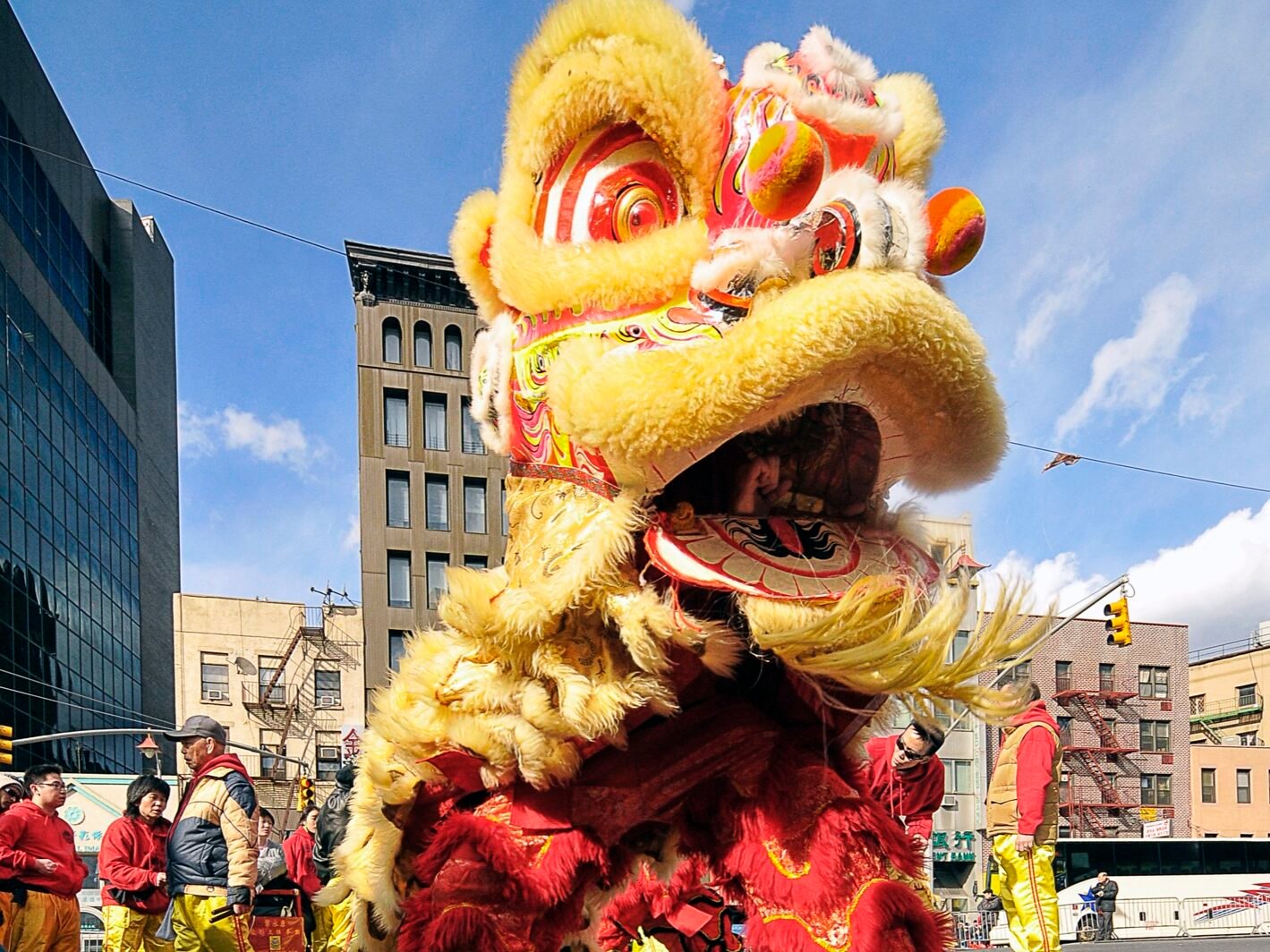 A vibrant Chinese lion dance performance taking place on a city street, with performers dressed in red and yellow traditional costumes.