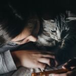 girl holding smartphone beside cat watching reclining to her shoulder