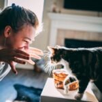 woman in gray sweater holding black and brown cat