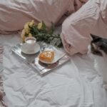 A relaxing morning scene with a cat, coffee, and flowers on a cozy bed.
