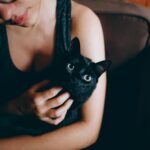 A young woman lovingly cuddles a black cat indoors, showcasing their bond.