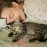 Woman and tabby kitten sleeping peacefully on floral bedding, embodying comfort and warmth.
