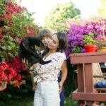 A couple enjoying time with their cat among colorful garden flowers.
