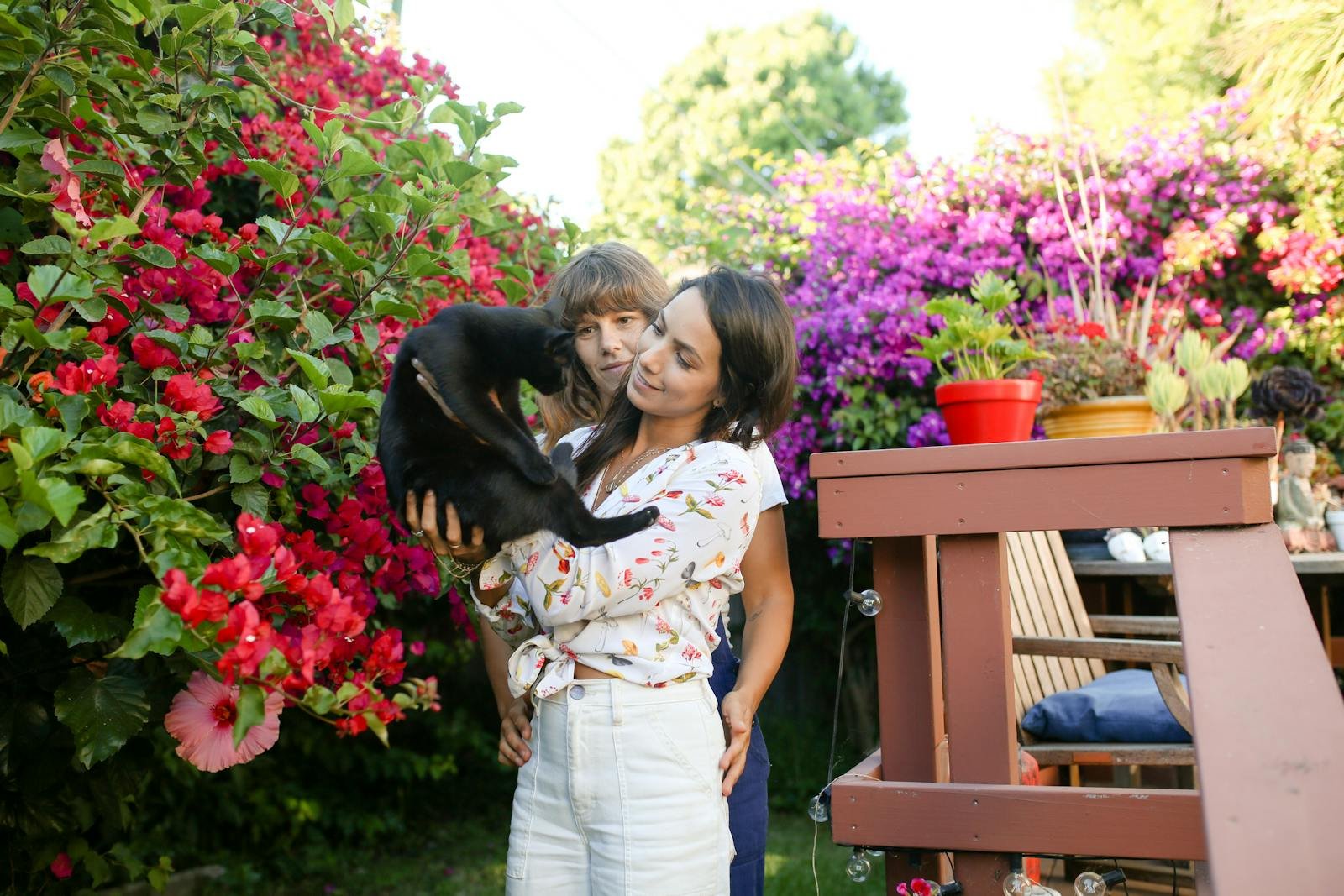 A couple enjoying time with their cat among colorful garden flowers.
