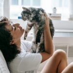 A woman cuddles her fluffy cat in a bright and cozy bedroom setting.