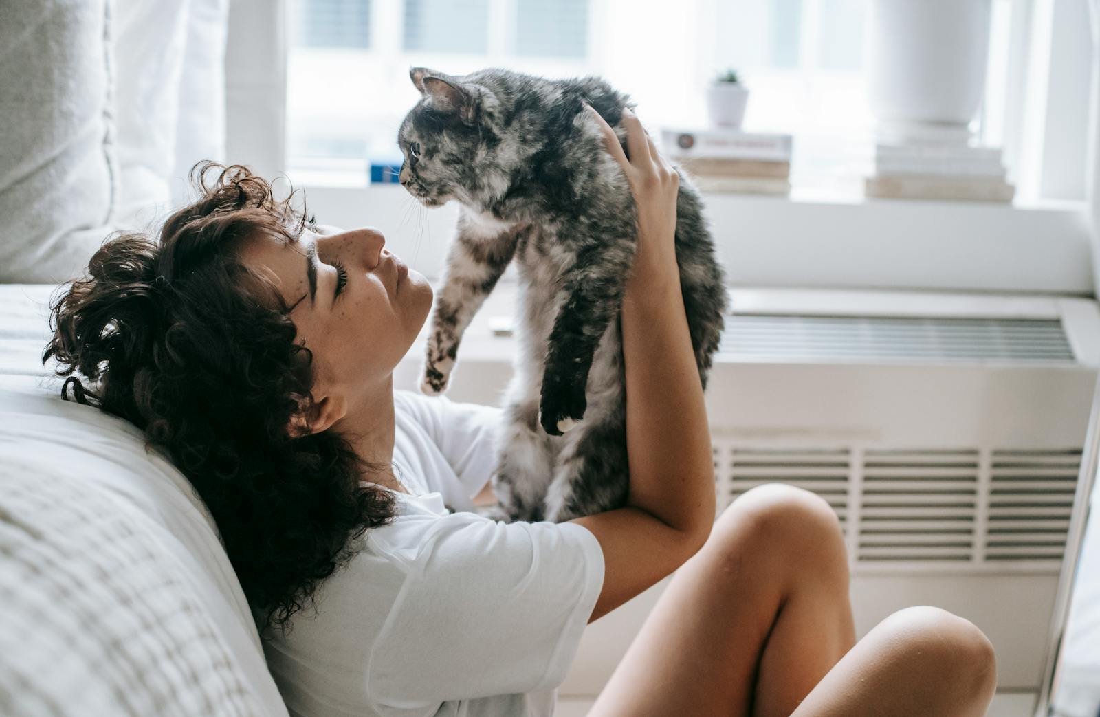 A woman cuddles her fluffy cat in a bright and cozy bedroom setting.