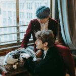 A couple shares a cozy moment with their cat by a large window in an urban apartment.