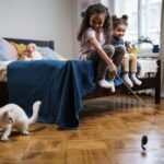 Two children playing with a white cat in a cozy bedroom setting, full of joy and laughter.