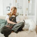 A cheerful teenager with headphones relaxing on a sofa with her dog, enjoying music indoors.