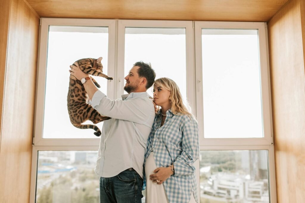 Pregnant woman and man enjoying time with Bengal cat indoors.