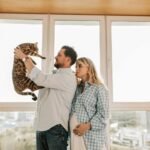 Pregnant woman and man enjoying time with Bengal cat indoors.