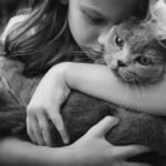 A young girl lovingly embraces a cat in a black and white image, capturing warmth.