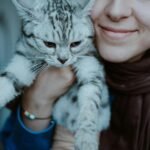 A woman joyfully holds her British Shorthair cat indoors.