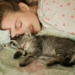 Woman and tabby kitten sleeping peacefully on floral bedding, embodying comfort and warmth.