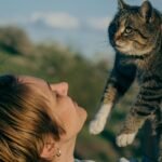 A woman holds a tabby cat outdoors in a sunny spring setting, emphasizing a loving connection.