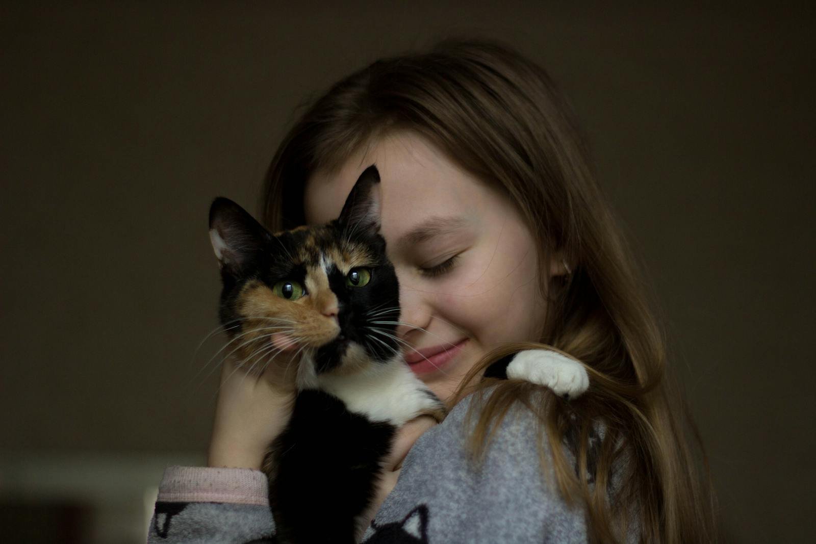 A young girl lovingly hugs a calico cat indoors, showing affection and friendship.