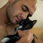 A man gently holds a black and white cat in an intimate moment of affection.