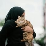 Middle Eastern woman holding a fluffy cat outdoors, wearing a hijab.