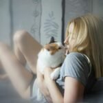 A young woman lovingly embraces her cat on the bed, capturing a moment of tranquility and affection.