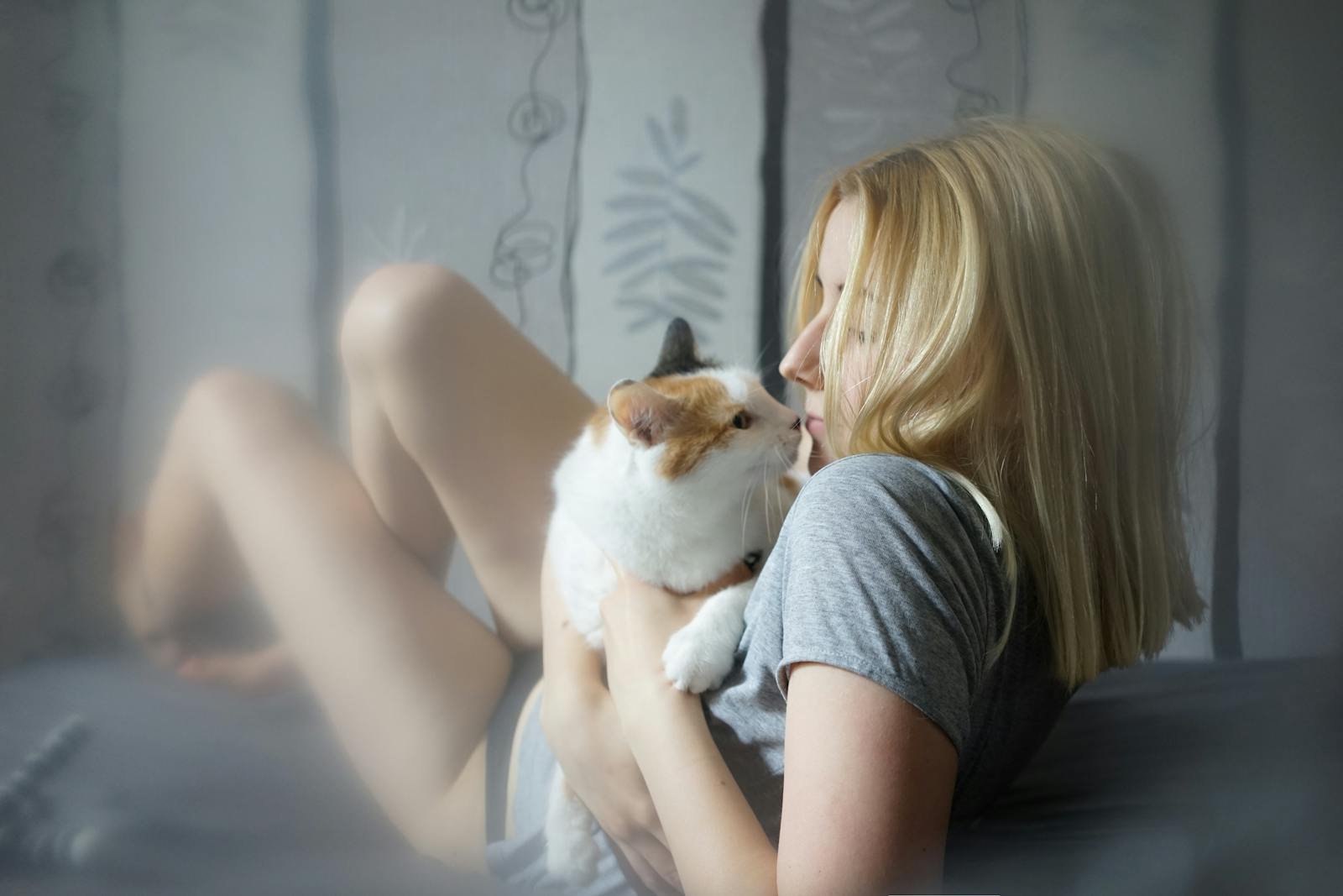 A young woman lovingly embraces her cat on the bed, capturing a moment of tranquility and affection.